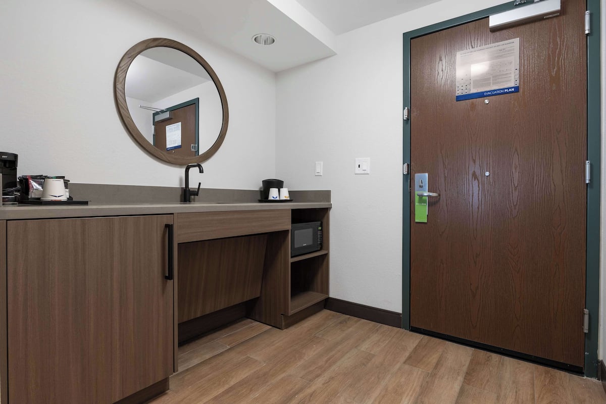 Quarto de hotel com uma penteadeira de madeira, micro-ondas, cafeteira e porta com sinal de plano de evacuação.