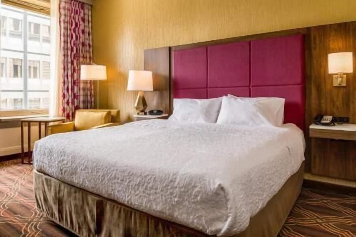 A hotel room with a large bed, two bedside tables, a chair, and a window with curtains.