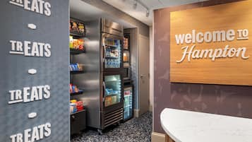 A hotel reception area with a wall sign reading 'welcome to Hampton' and a wall-mounted sign indicating a treats section.