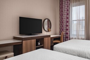 A hotel room with a flat-screen TV, a round mirror, a desk with a coffee machine, and two beds. - Hampton Inn Majestic Chicago Theatre District (Chicago)
