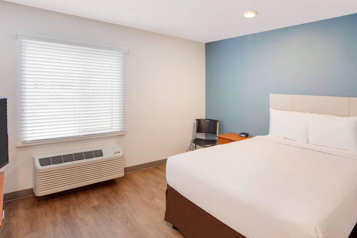 Ein Hotelzimmer mit Bett, Schreibtisch, Stuhl, Heizung und einem Fenster mit Jalousien.