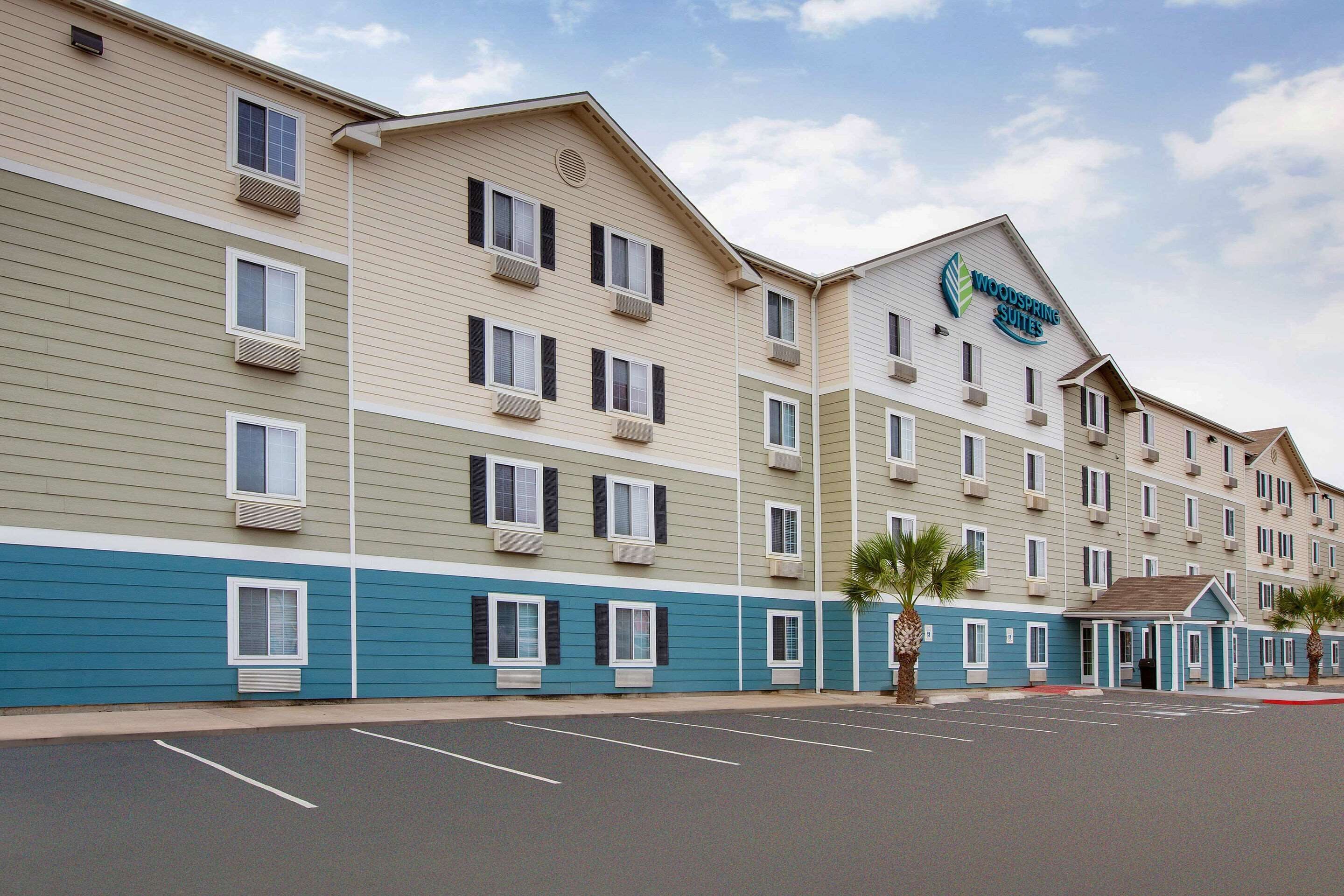A multi-story hotel with a flat roof and a sign for 'Woodspring Suites'.