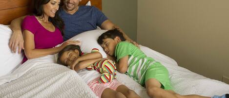 A family of three sleeping in a bedroom with a wooden headboard and white bedding.