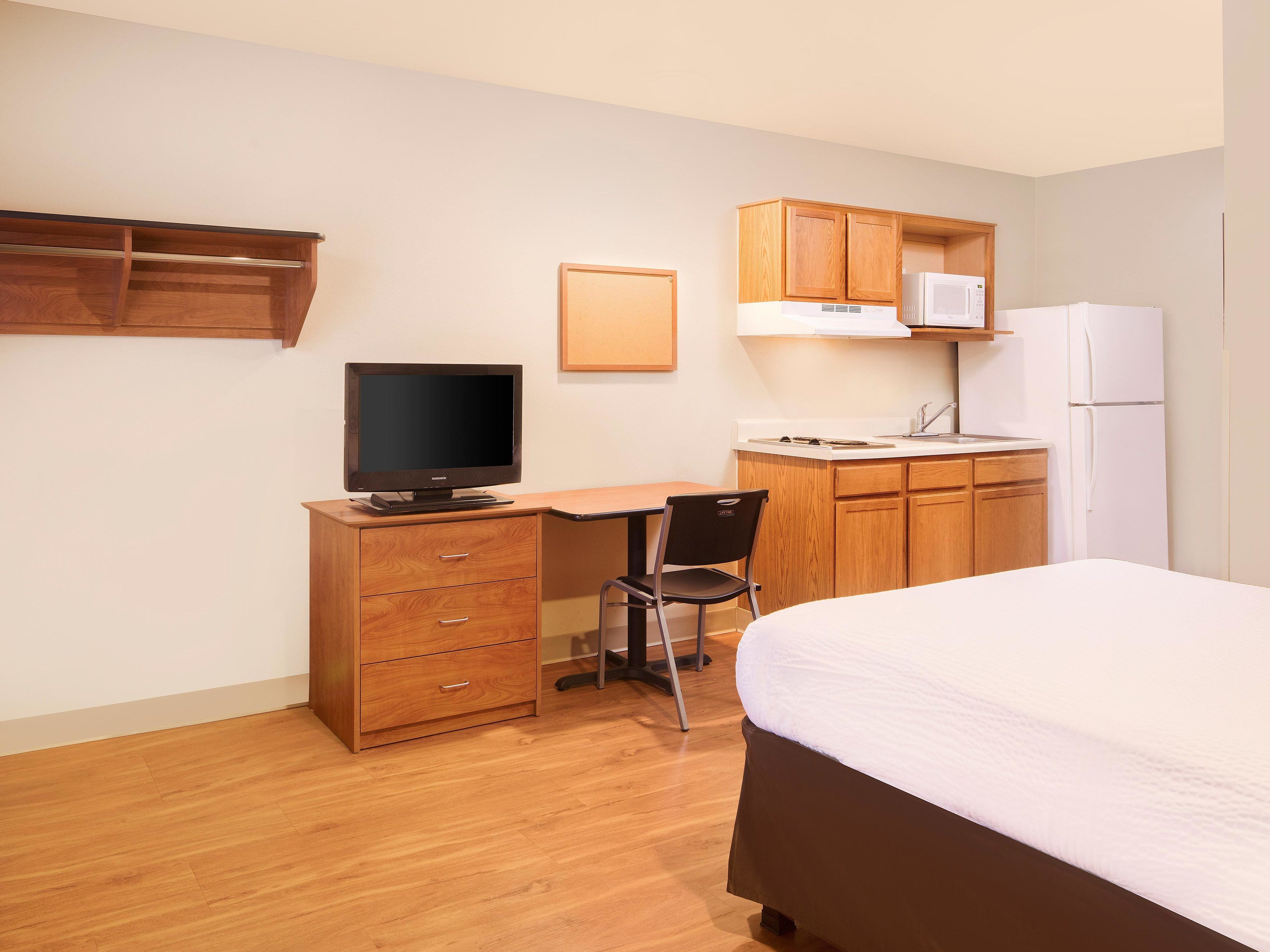 Habitación de hotel pequeña con cama, escritorio con computadora, silla, kitchenette y televisión.