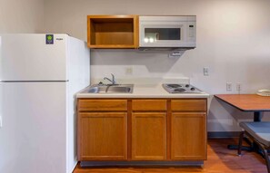 A compact kitchen with a refrigerator, microwave, sink, and wooden cabinets. - Extended Stay America Select Suites - Fayetteville - Cliffdale (Fayetteville)