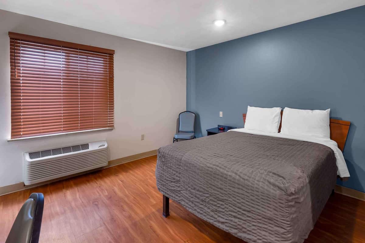 A bedroom with a bed, a chair, a heater, and a window with blinds.
