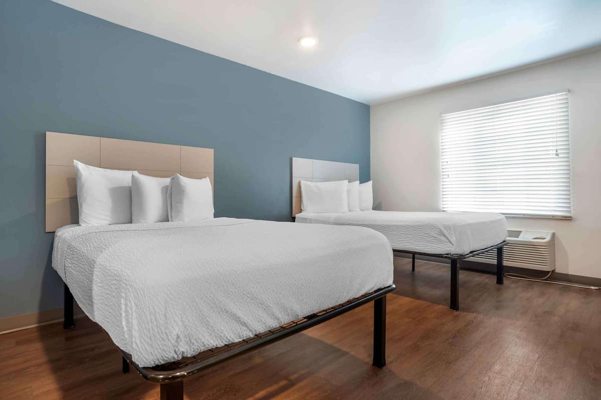 Two single beds with headboards, a window with blinds, and a wooden floor.