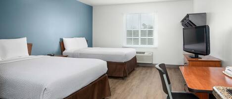 Een hotelkamer met twee bedden, een bureau, een stoel, een televisie en een raam met jaloezieën.