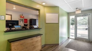 A reception area with a counter, a wooden desk, a wall-mounted phone, and a door leading outside. - Extended Stay America Select Suites - Pensacola - Northeast (Pensacola)