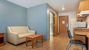 A compact living space with a sofa, a small table, a kitchenette with a fridge and microwave, and a door leading to a bathroom. - Extended Stay America Select Suites - Pensacola - Northeast (Pensacola)