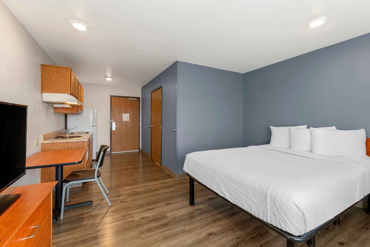 A hotel room with a bed, a desk with a chair, a television, and a kitchenette.