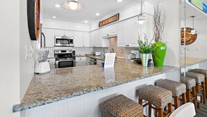 Una cocina moderna con armarios blancos, encimera de granito y una zona de bar con taburetes de mimbre.
