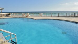 Una piscina con vista al océano, rodeada de tumbonas y una barandilla.