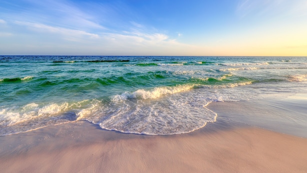 Una playa con olas que acarician suavemente la orilla bajo un cielo despejado.