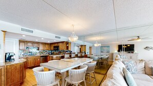Un vaste espace de vie comprenant un grand canapé, une table à manger avec des chaises, et une cuisine avec des meubles en bois et un grand îlot central.