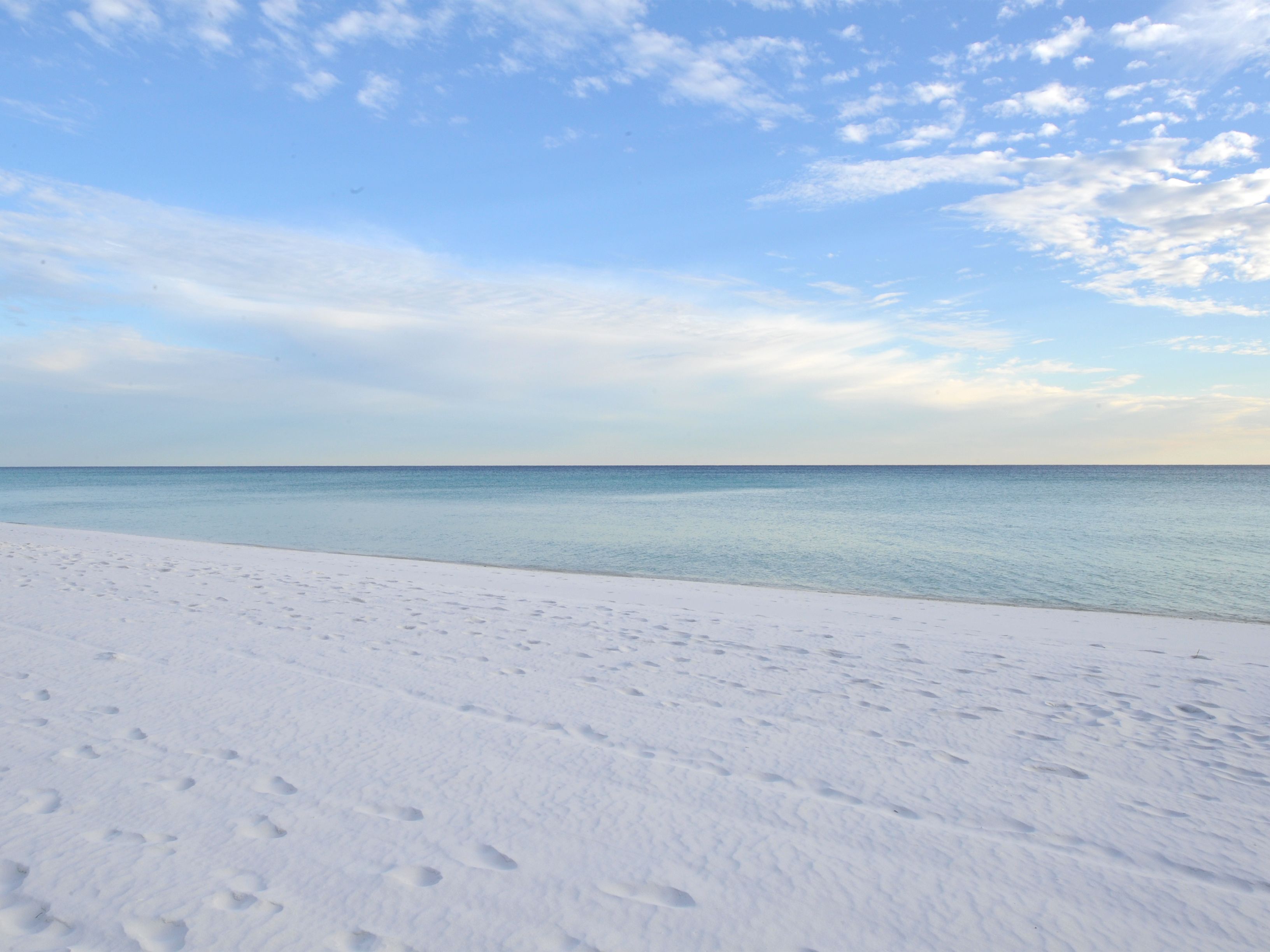 Una playa de arena blanca y mar tranquilo bajo un cielo parcialmente nublado.