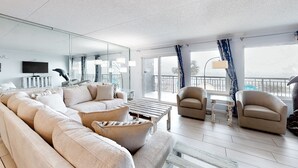 Un salon moderne avec un grand canapé, des fauteuils, une table basse et un balcon offrant une vue agréable.