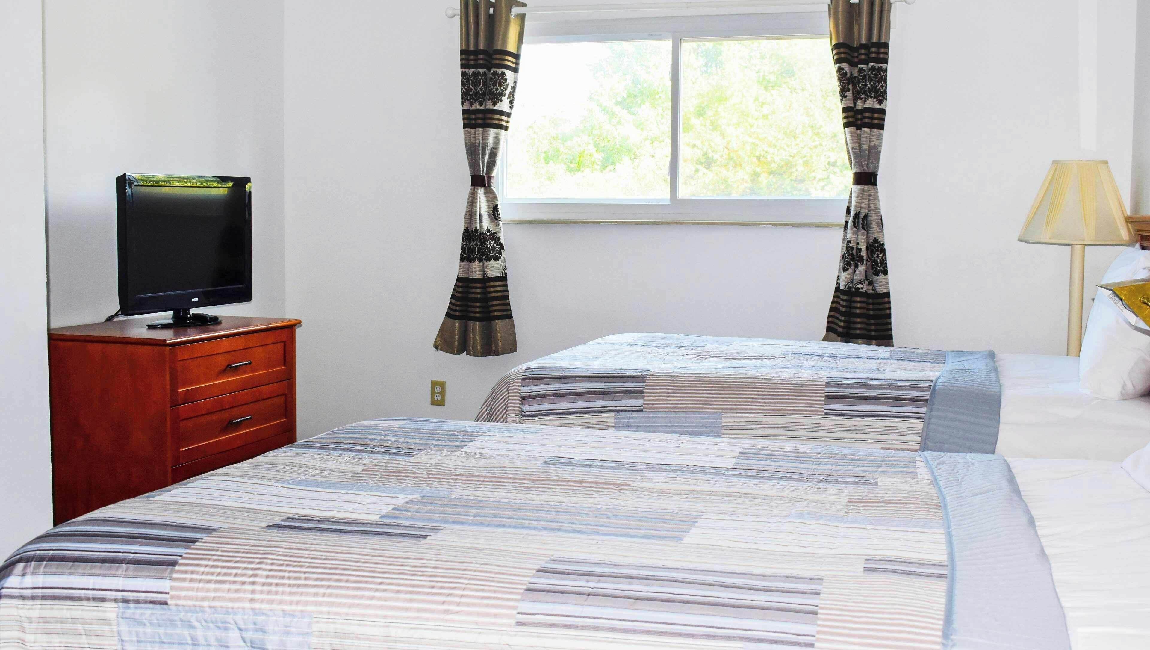 Une chambre à coucher avec un lit, un téléviseur posé sur une commode en bois et des rideaux à la fenêtre.