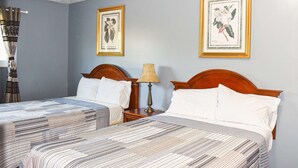 Quarto de hotel com duas camas, uma mesinha de cabeceira com abajur e duas gravuras emolduradas com motivos botânicos na parede.