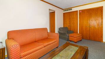 A room with a polka-dotted orange sofa, a striped armchair, and a wooden cabinet with two doors.