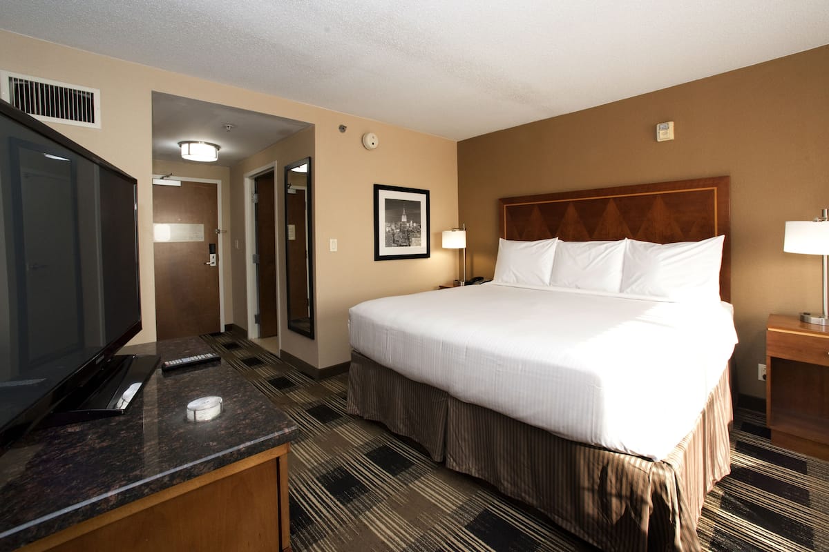 A hotel room with a large bed, a television, a desk, and a lamp.
