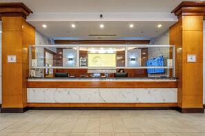 A hotel reception desk with a marble counter, a computer monitor, and a television screen displaying a room view. - Hotel Executive Suites Newark Liberty Int'l Airport Carteret (EWR) (Carteret)