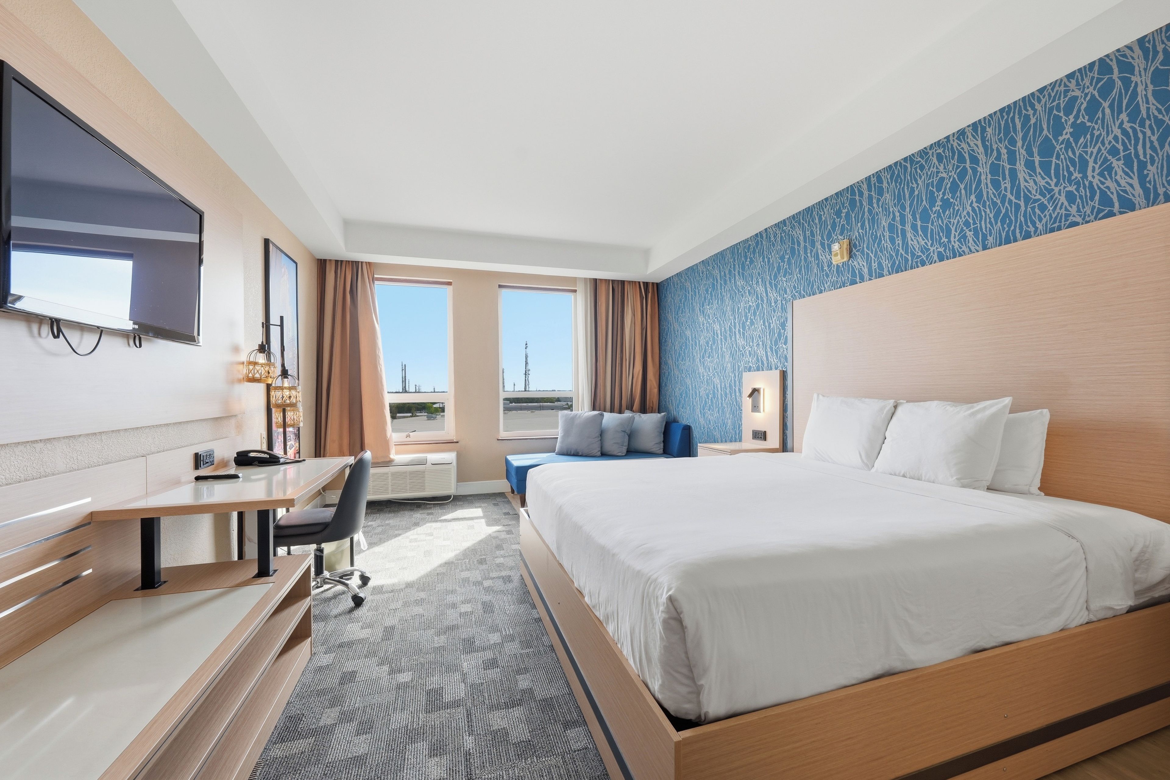 A hotel room with a bed, desk, chair, and a view of the cityscape.