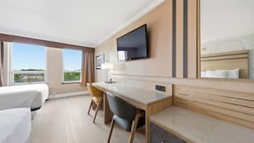 Habitación de hotel con cama, escritorio, silla, televisor y ventana grande con vistas.