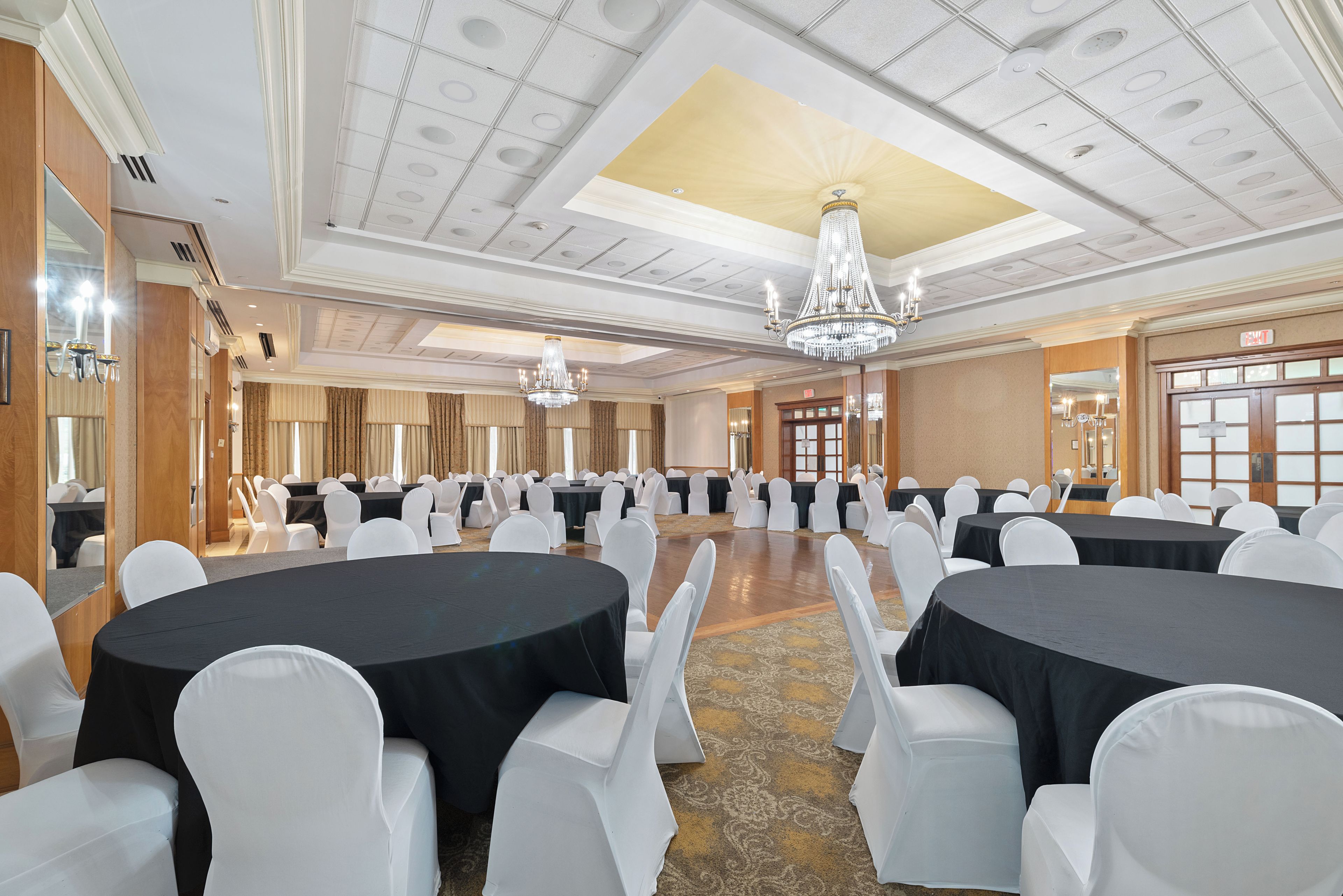 Un salón de conferencias con mesas redondas, sillas blancas, candelabros y una alfombra estampada.