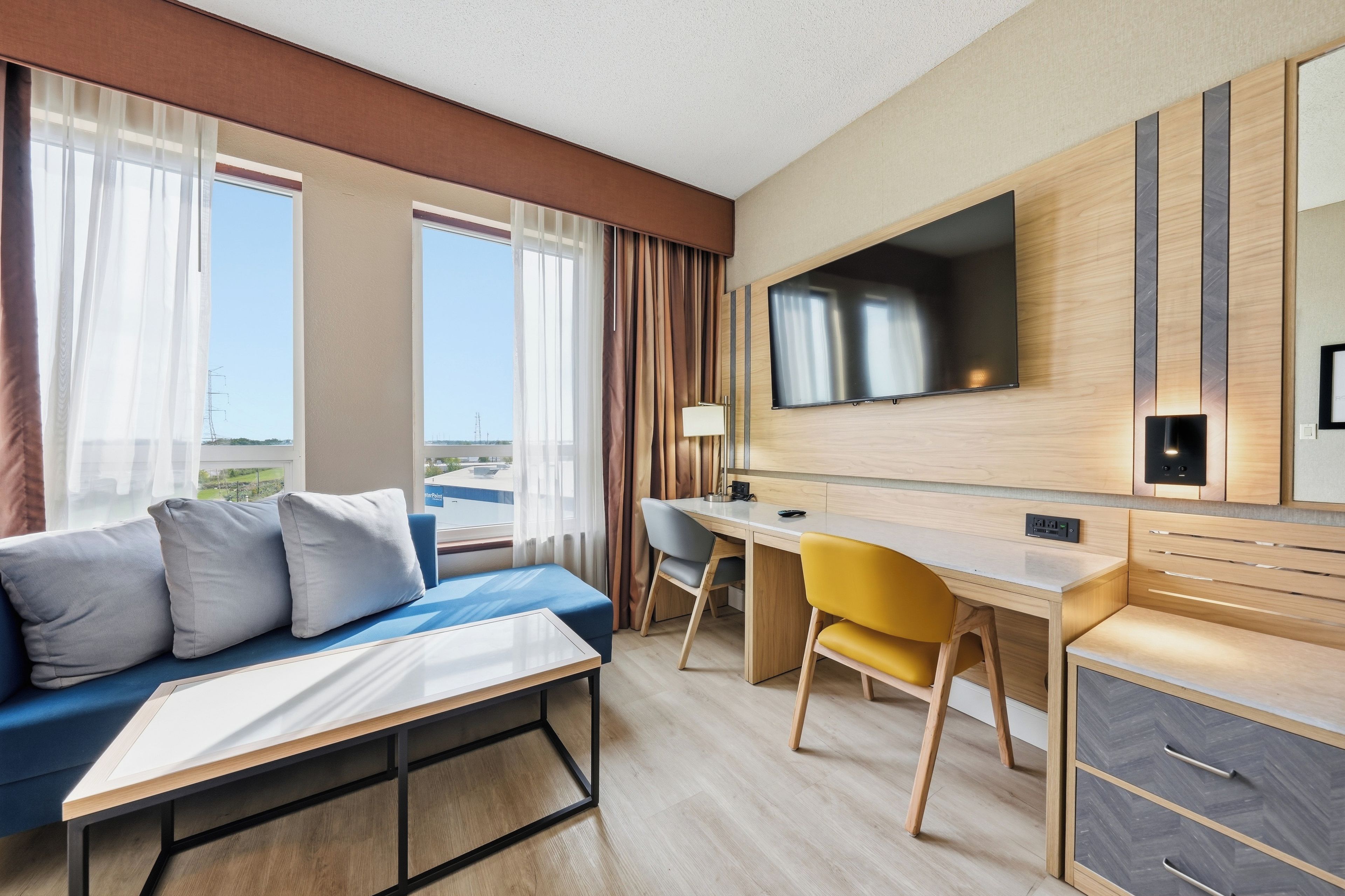 Habitación de hotel con cama, escritorio, silla, televisor y vistas al exterior.