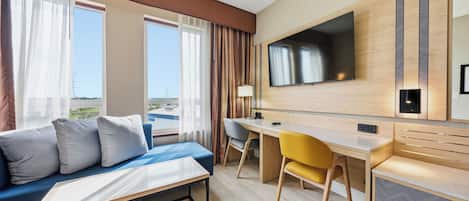 A hotel room with a bed, a desk, a chair, a TV, and a view of the outdoors.