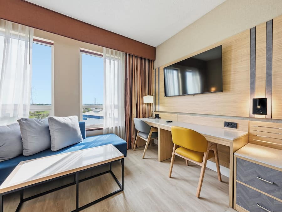 A hotel room with a bed, a desk, a chair, a TV, and a view of the outdoors.