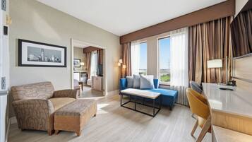 Habitación de hotel con sofá, una mesita, un escritorio y vistas al exterior.