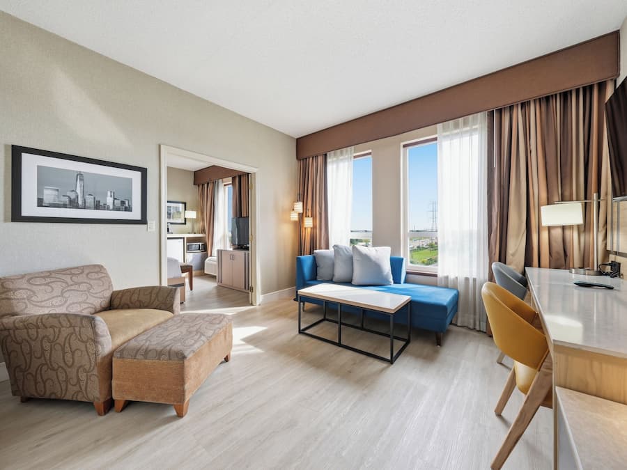 A hotel room with a sofa, a small table, a desk, and a view of the outdoors.