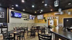 Interior de restaurante con varias mesas y sillas, un televisor montado en la pared y una señal de salida.