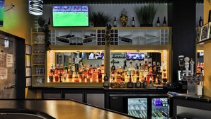 A bar area with shelves of liquor bottles, a television displaying a sports event, and a counter with a cash register. - Hotel Executive Suites Newark Liberty Int'l Airport Carteret (EWR) (Carteret)