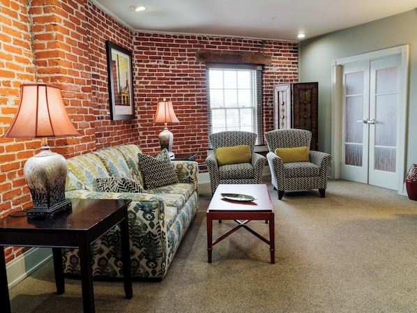 A living room with a brick wall, two patterned armchairs, a sofa, a coffee table, and a lamp.