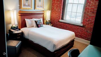 A hotel room with a bed, a nightstand, a lamp, a chair, and a window with blinds.