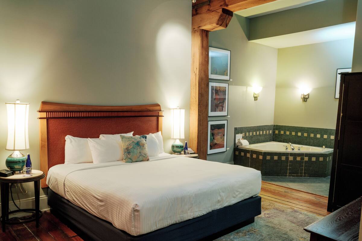 Una habitación de hotel con una cama grande, un área de descanso, una bañera y obras de arte en las paredes.