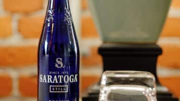 A blue bottle labeled 'Saratoga' and a clear glass on a table with a brick wall in the background.