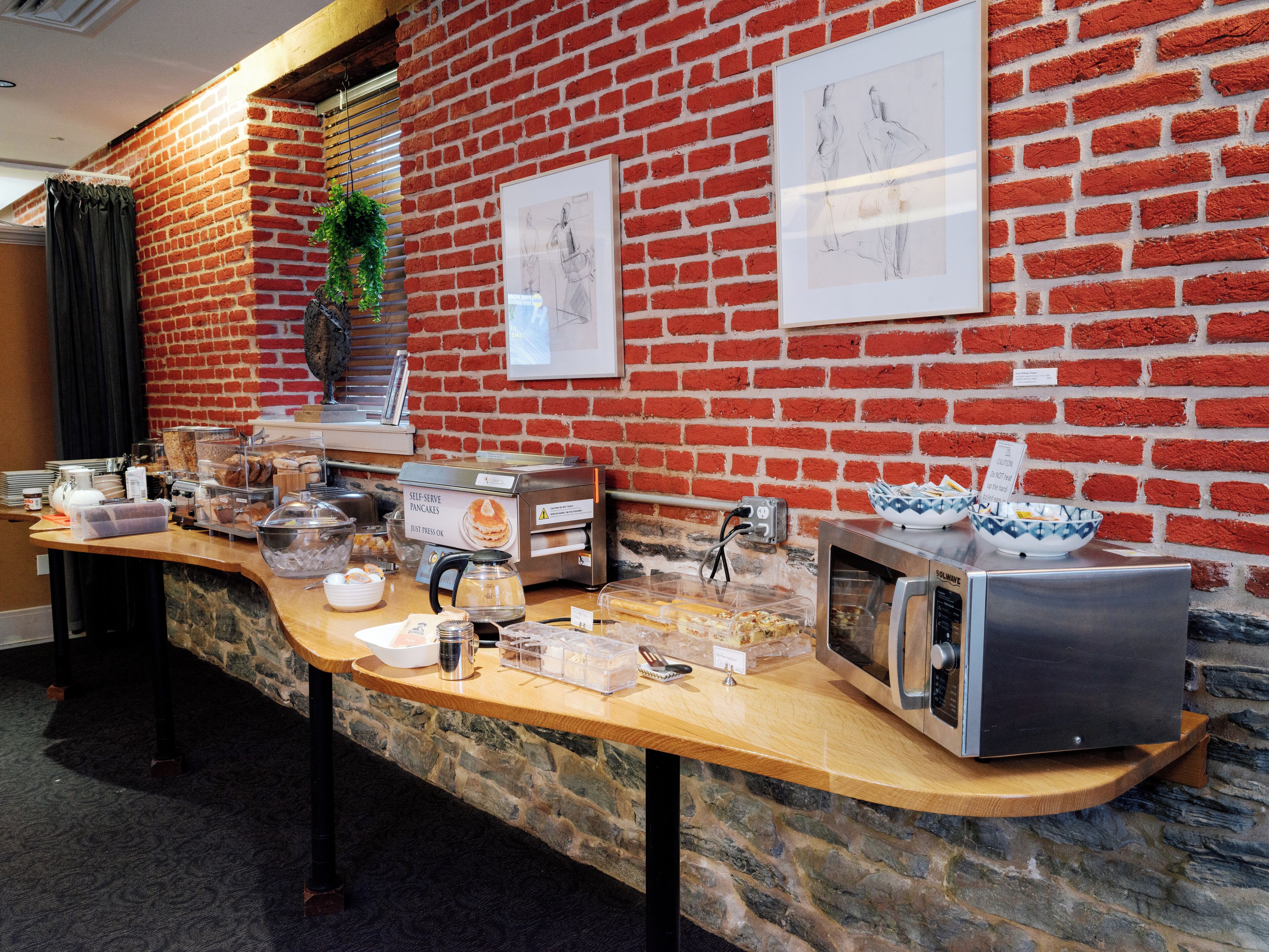 Un bar de cuisine avec une machine à café, un grille-pain et un four à micro-ondes, le tout installé devant un mur de briques orné d’œuvres d’art.