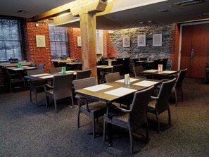 A restaurant with brick walls, stone accents, and wicker furniture. Tables are set with menus and place settings.