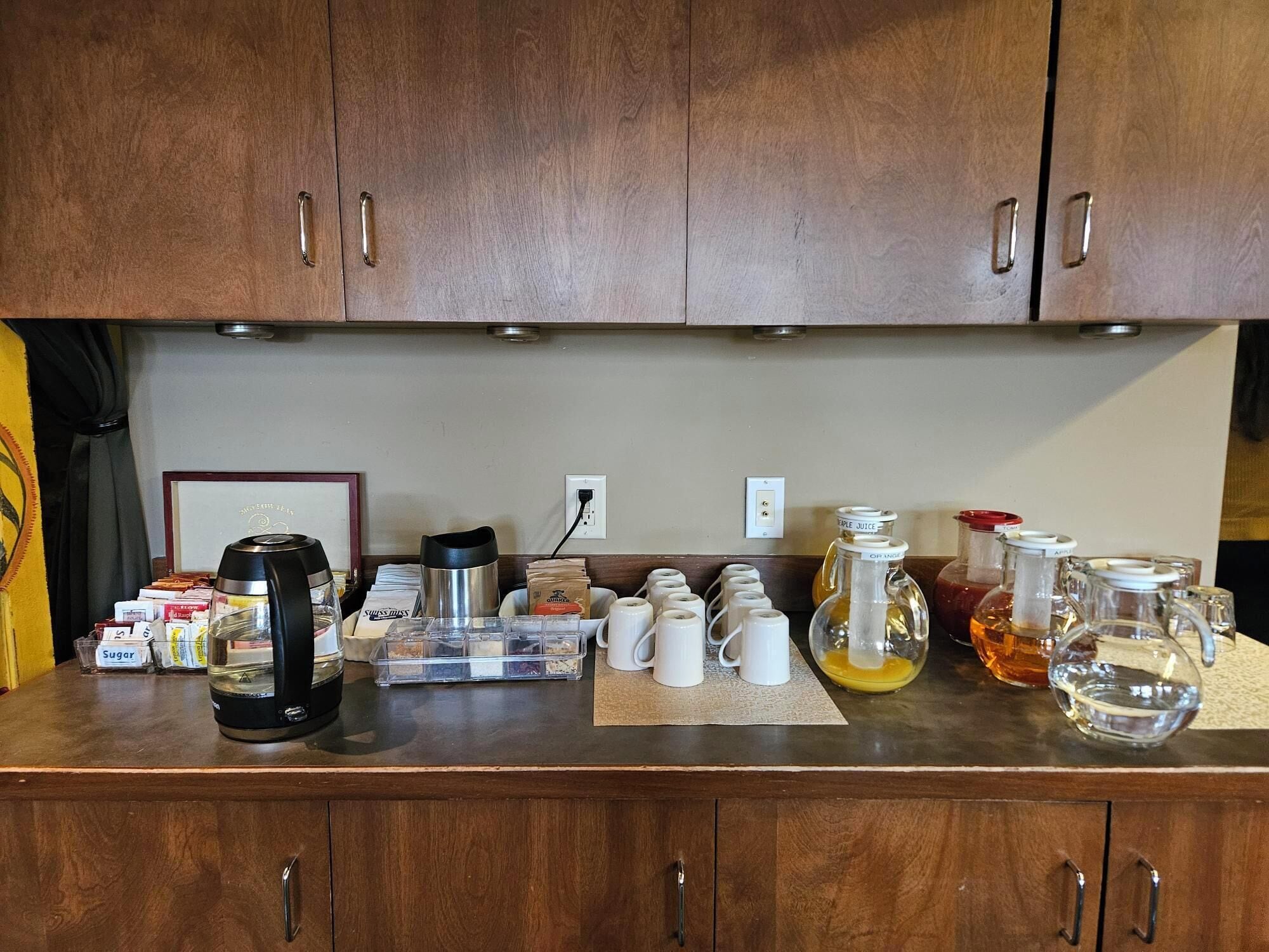 A kitchen counter with various items including a coffee maker, sugar packets, a thermos, and glass containers.