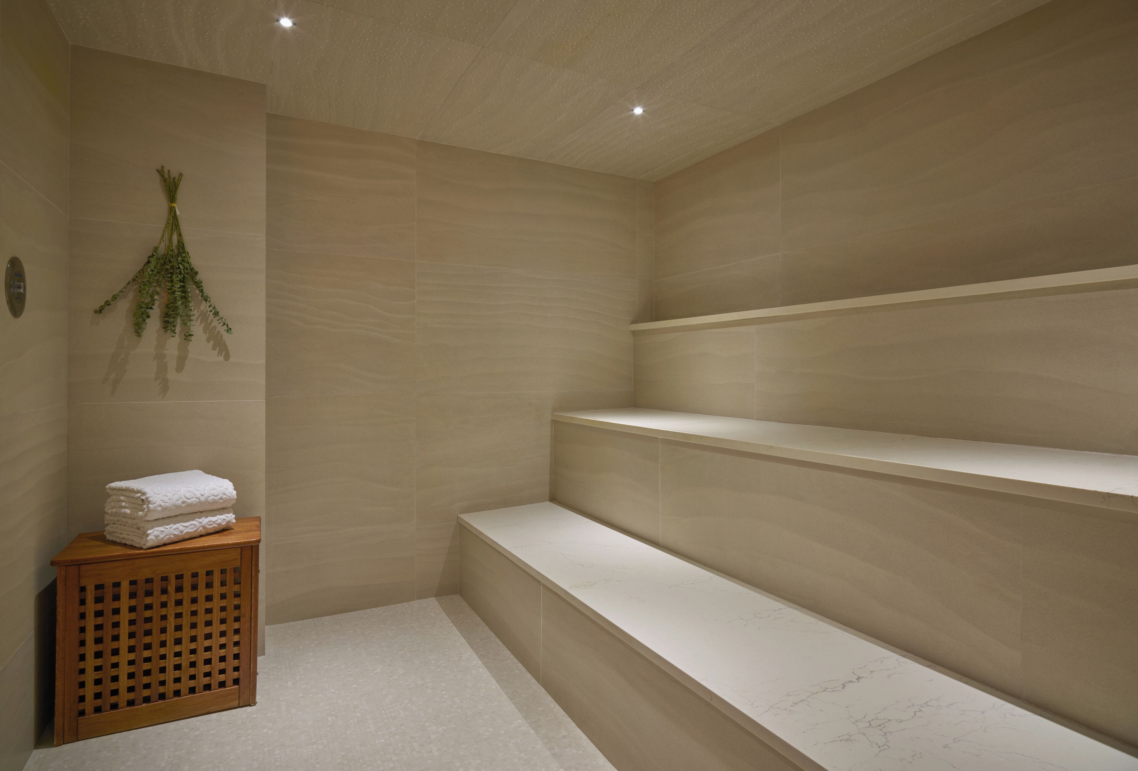 A spa room with a wooden bench, a small wooden table with towels, and a wall-mounted plant.