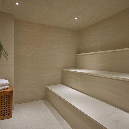 A spa room with a wooden bench, a small wooden table with towels, and a wall-mounted plant.