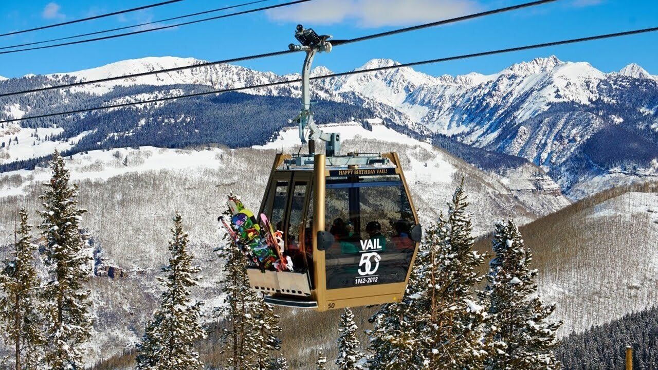A cable car with "HAPPY BIRTHDAY VAIL" and "VAIL 50 1962-2012" signage, moving through a snowy mountain landscape.