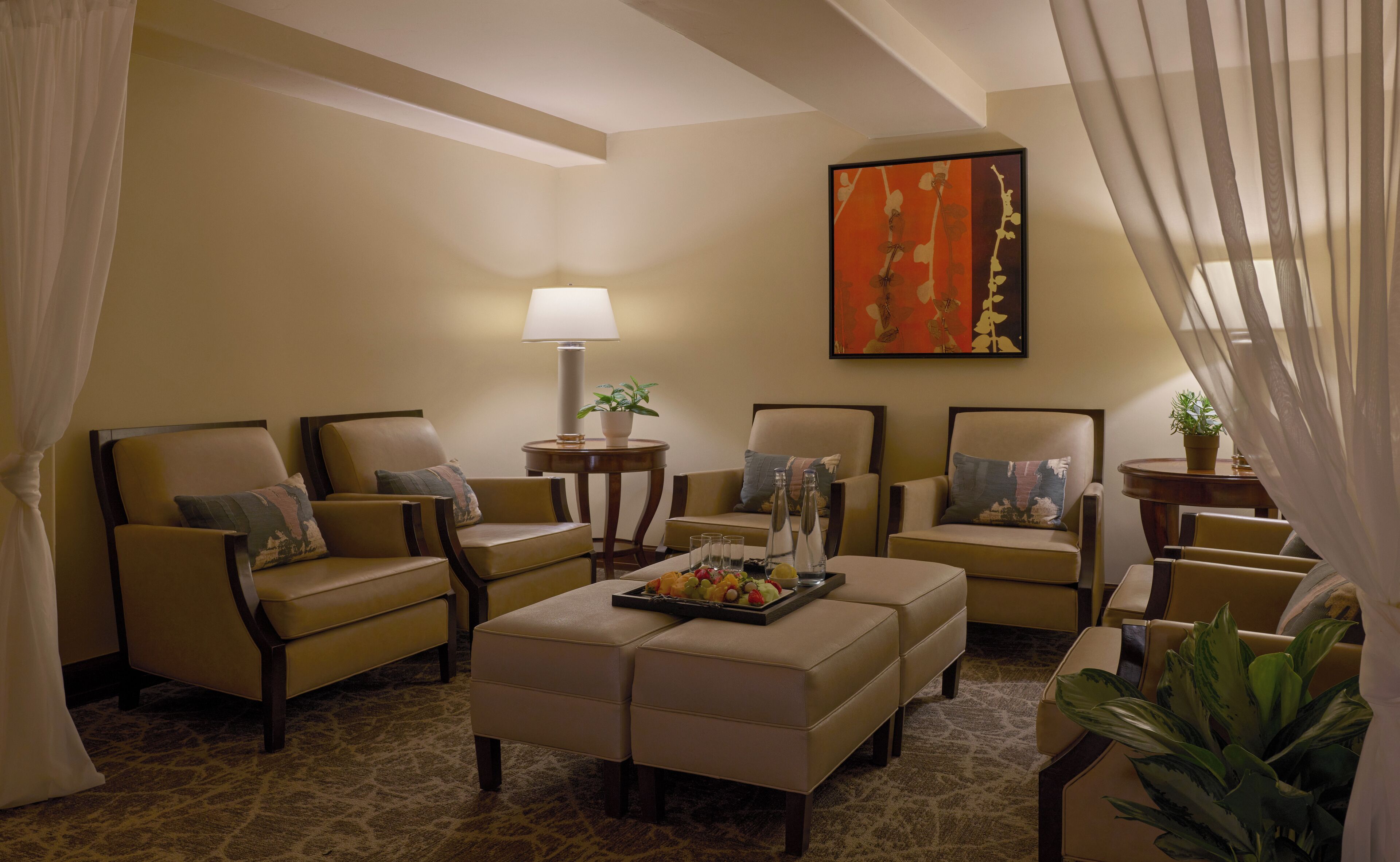 Habitación de hotel con sofá, una mesita de centro con fruta, una lámpara y un cuadro en la pared.