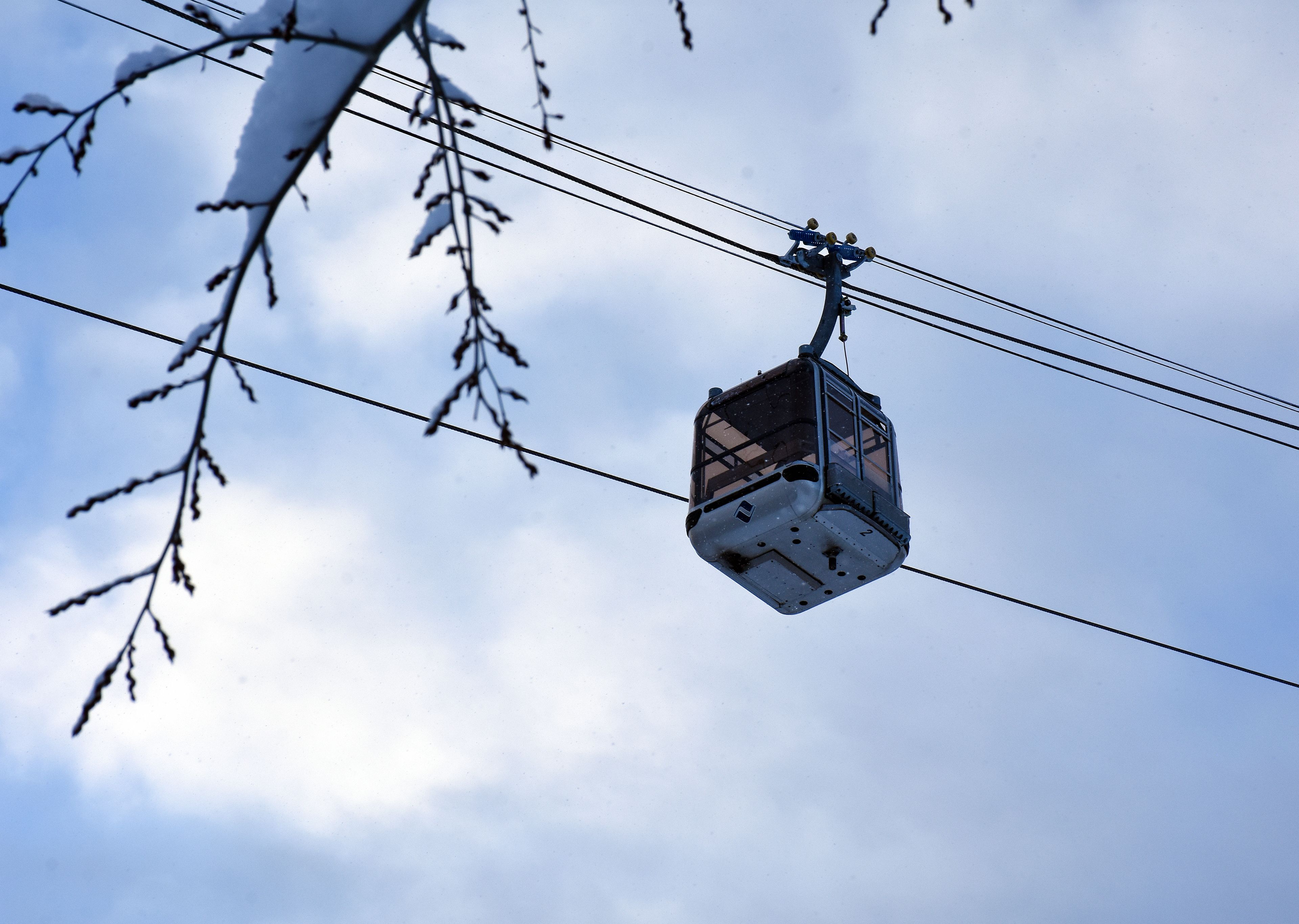 A cable car suspended between power lines, with snow-covered branches in the foreground.