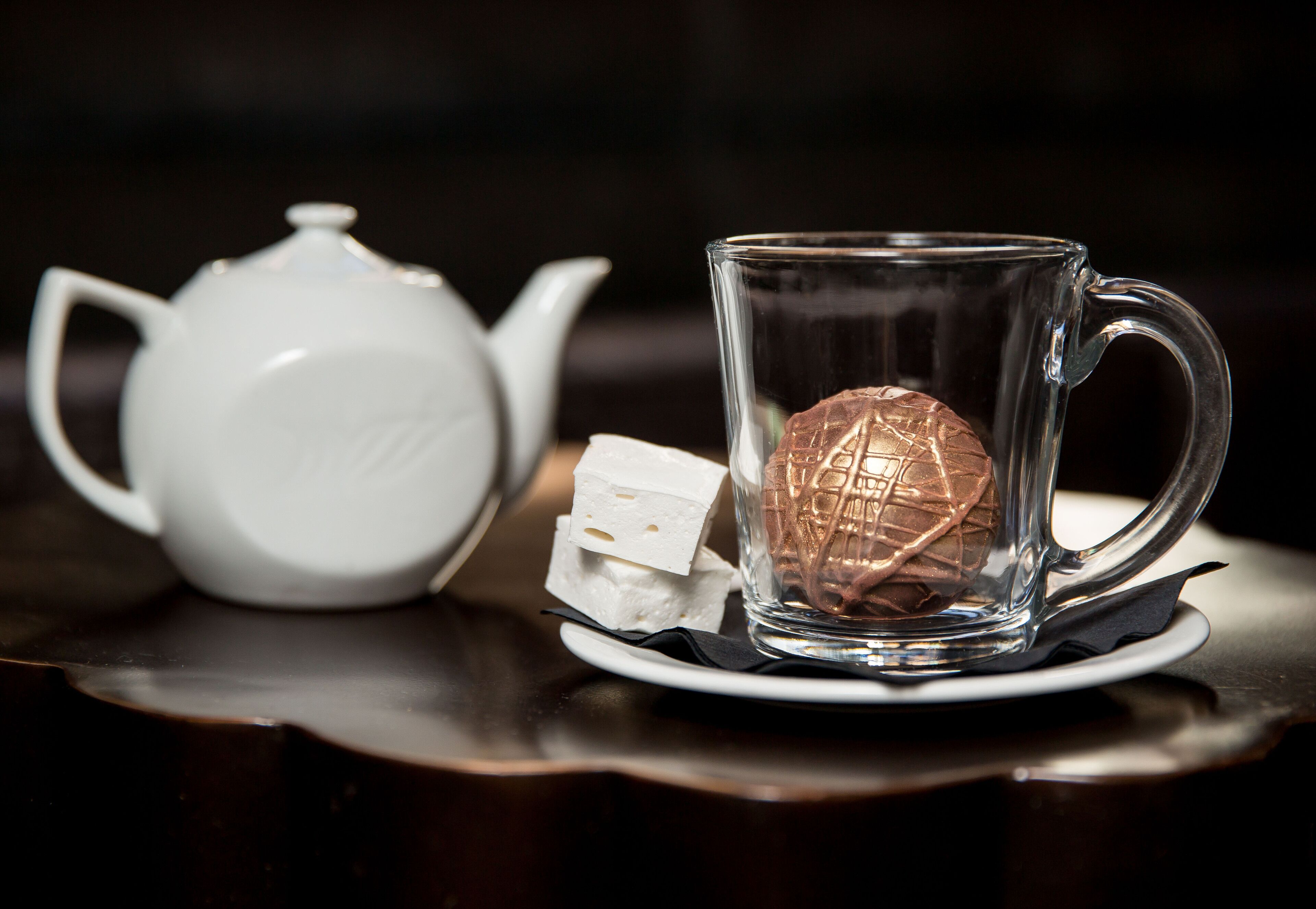 A clear glass teapot and mug on a dark wooden table.