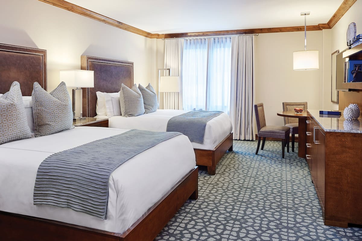 A hotel room with two beds, a desk, a chair, a dresser, and a large window with curtains.